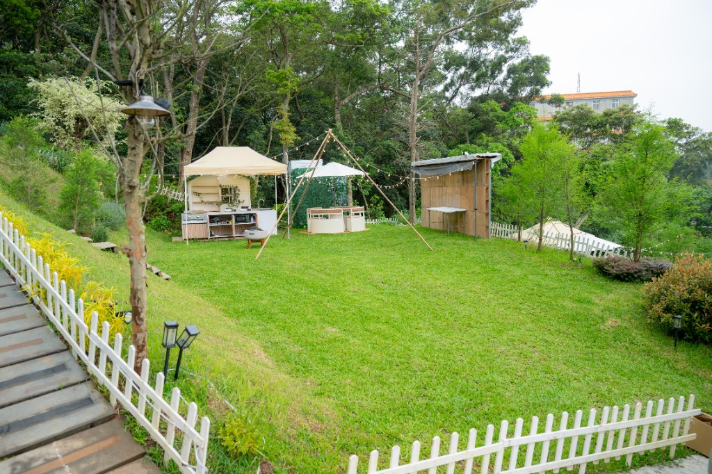 熱氣球房專屬草地全景，白色柵欄、森林背景、小木屋戶外廚房與花牆，桃園楊梅森林豪華露營包場｜揪好森